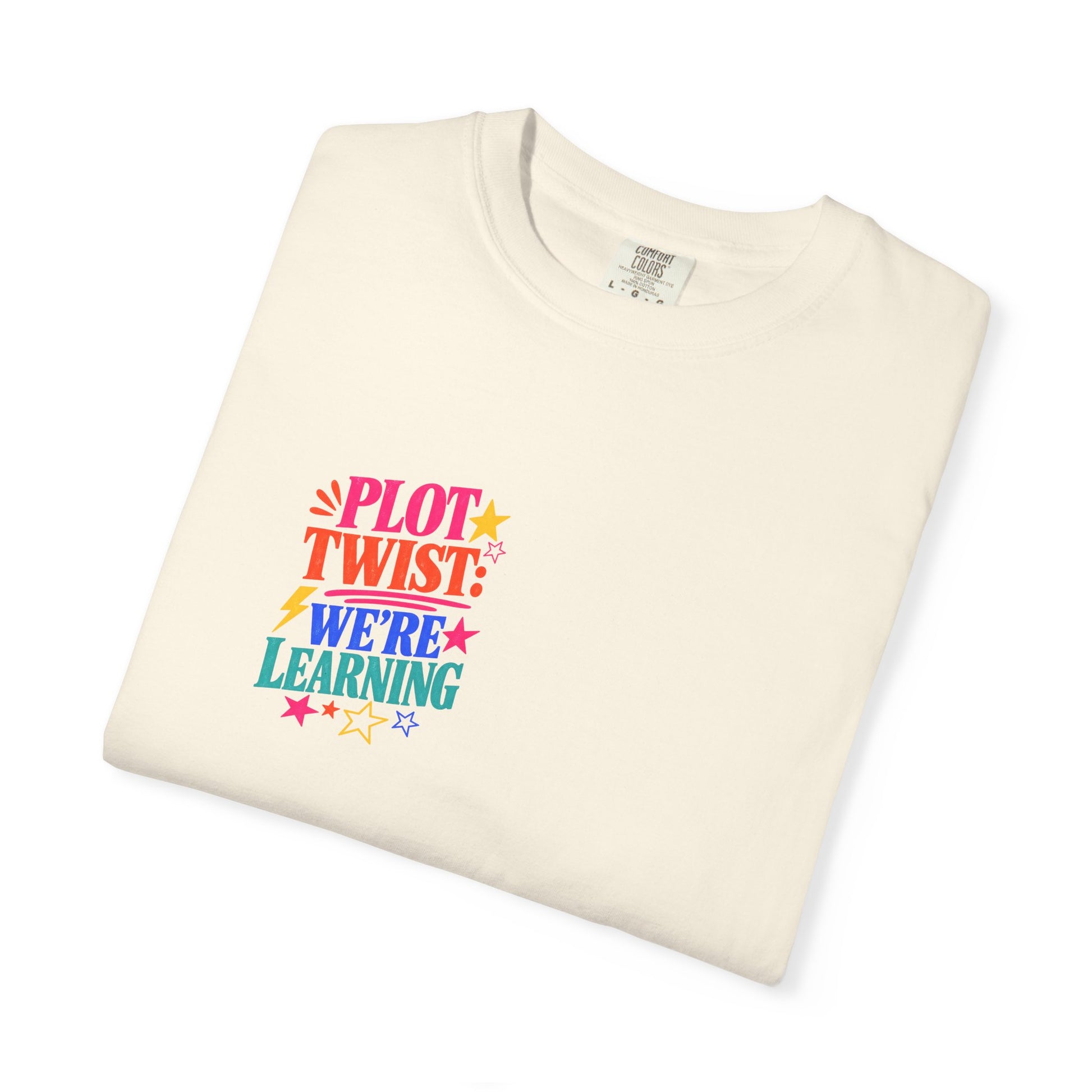Plot Twist: We're Learning Tee in Ivory, folded flat - a small left-chest print on a garment-dyed Comfort Colors 1717 tee.